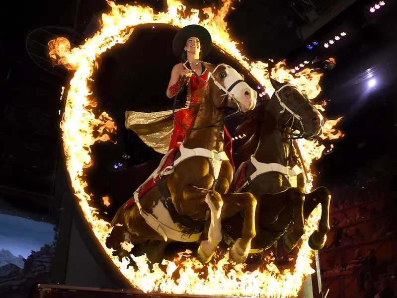trick rider and horses leaping through ring of fire