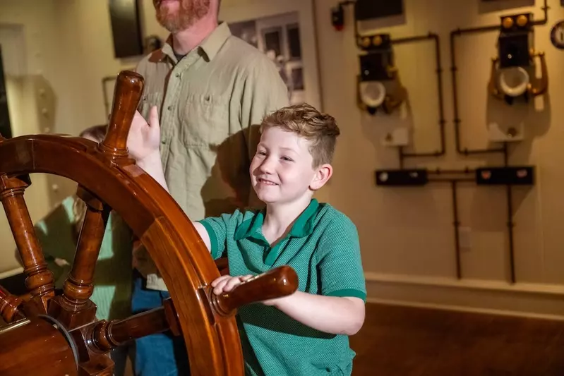 smiling kid steering the ship at the Titanic Museum in Branson